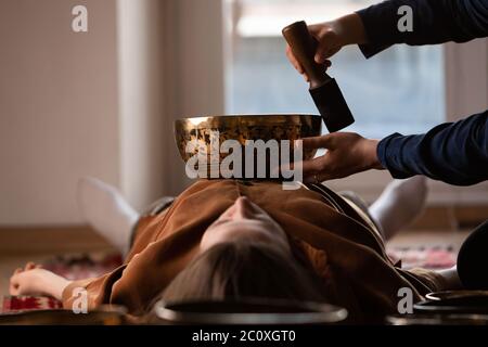 Femme faisant massage relaxant, méditation, thérapie sonore avec des bols de chant tibétien. Soulagement de stress. Mise au point sélective sur la face femelle. Vue de dessous. Banque D'Images