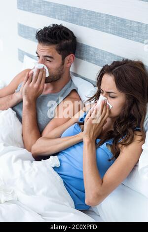 High angle view of young couple couvrant nez pendant l'éternuement on bed Banque D'Images