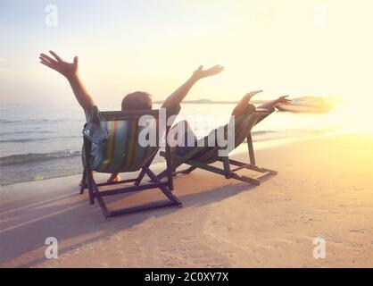 Heureux couple assis aux chaises longues sur la plage de Koh Samet au coucher du soleil Banque D'Images