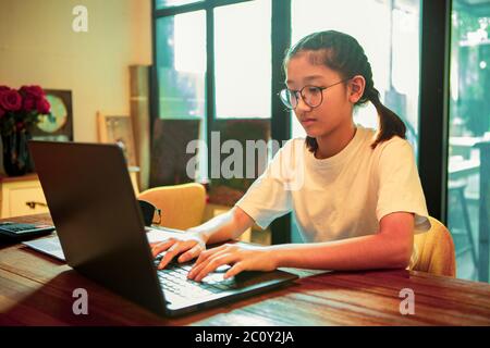 adolescent asiatique assis dans le salon et dactylographiant sur ordinateur portable Banque D'Images