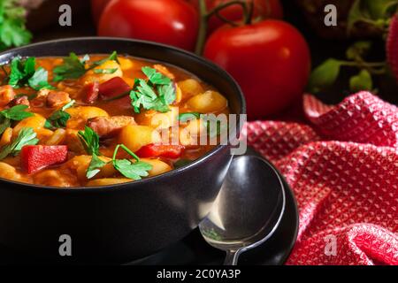 Soupe de haricots blancs avec pommes de terre, tomates, paprika et bacon dans un bol en céramique noire Banque D'Images