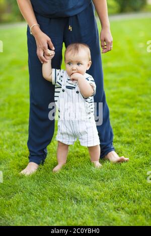 Bébé apprenant à marcher à l'extérieur. Mère heureuse et son fils jouant ensemble dans le parc Banque D'Images