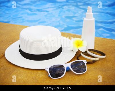 Crème solaire, lunettes de soleil, chapeau, bracelet près de la piscine Banque D'Images