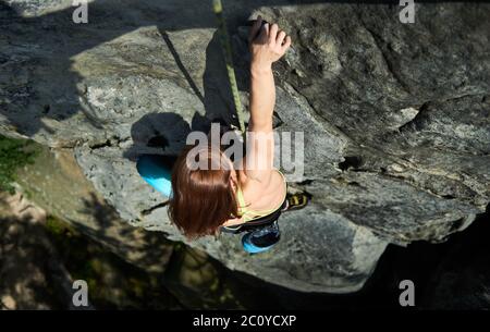 Photo horizontale de la jolie femme dans le harnais de sécurité, monter la roche avec la corde, faisant l'étape suivante en aidant avec une main. Vue de dessus. Concept de sport de montagne, escalade Banque D'Images