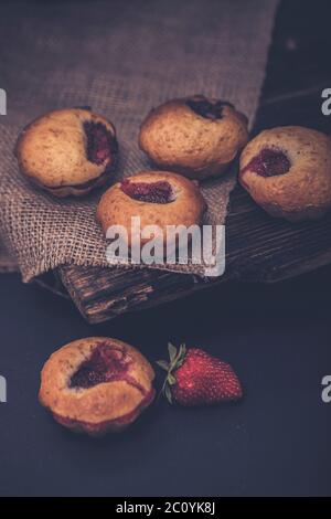 Cupcakes à la crème blanche et aux fraises sur une couverture vintage sur fond de bois noir et fraises fraîches. Banque D'Images