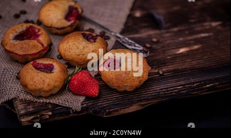 Muffin aux fraises et grains de café sur un panneau en bois sur fond de bois sombre. Muffins au chocolat sur fond sombre, mise au point sélective. Banque D'Images