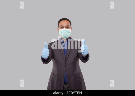 Homme d'affaires montrant des deux mains de Thbomp Up portant un masque médical et des gants isolés. Panneau Indian Business Man Standing Thump Up Banque D'Images