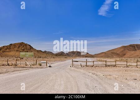 Panneau indiquant l'entrée du parc national Namib Naukluft en Namibie. Route de gravier, porte d'entrée, clôture en bois, ciel bleu, chaude journée ensoleillée Banque D'Images