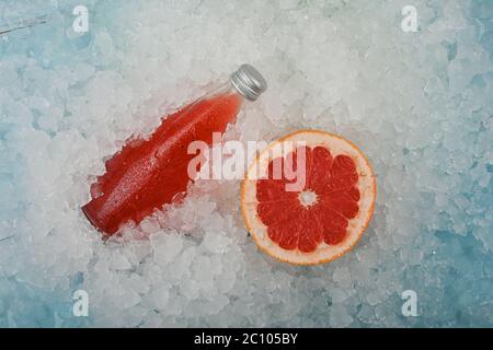 Fermez une bouteille de verre de boisson froide pour cocktail de jus rouge avec des graines de chia et du pamplemousse rose demi-coupé sur de la glace pilée sur un présentoir de vente au détail, un hig élevé Banque D'Images