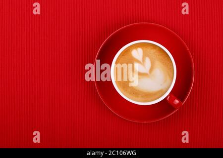 Fermez une tasse de café cappuccino sur la soucoupe rouge au-dessus de la nappe rouge, vue en hauteur, directement au-dessus Banque D'Images