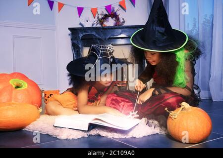 Deux filles lisent le livre d'assistant en Halloween sorcières de lancer un sort avec baguette magique tenant assis près de la cheminée Banque D'Images