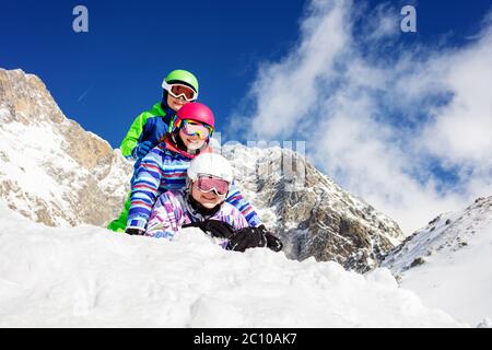 Portrait de trois enfants heureux se sont couché l'un sur l'autre dans la neige souriant avec des montagnes sur le fond Banque D'Images