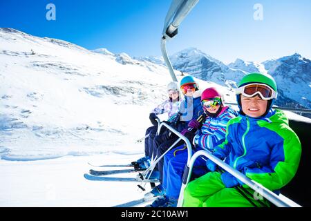 Portrait de quatre enfants heureux dans des vêtements de ski vif se levant sur le télésiège sur la montagne ensemble et souriant Banque D'Images