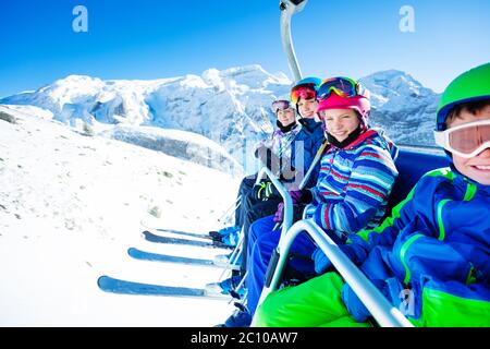 Un groupe d'enfants, amis skiables, s'assoient sur le télésiège au sommet de la montagne par beau temps Banque D'Images