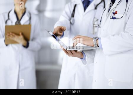 Un groupe de médecins, hommes et femmes inconnus, avec des stéthoscopes, discutent des examens médicaux, à l'aide d'un ordinateur portable, tout en se tenant au bureau de l'hôpital Banque D'Images