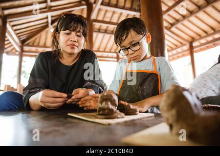 Mère aide son fils tout en jouant de l'artisanat en argile dans la galerie d'atelier de poterie Banque D'Images