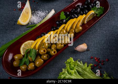 Variété d'olives vertes, noires et marinées mélangées dans un plat d'olivier sur une table en bois. Mise au point sélective Banque D'Images