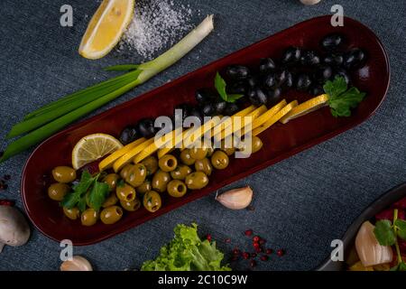 Variété d'olives vertes, noires et marinées mélangées dans un plat d'olivier sur une table en bois. Mise au point sélective Banque D'Images