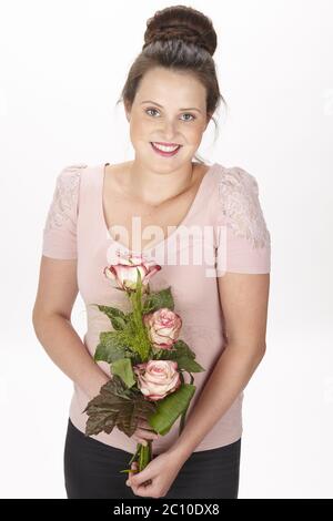 Jeune femme brune dans un chignon portant un bouquet de fleurs (roses) Banque D'Images