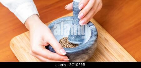 Mains de femme broyer du poivre noir par pilon dans un mortier de granit gris sur la table. Banque D'Images