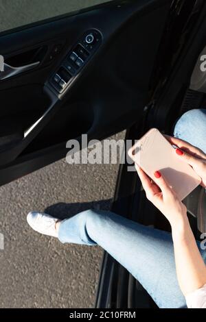 Une femme est entrée dans une voiture et a laissé tomber un smartphone sur l'asphalte, a cassé la vitre sur le couvercle arrière, vue de dessus. Ramassage du téléphone cassé par le sol. Banque D'Images