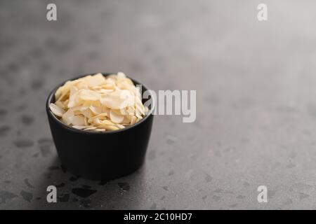 Flocons d'amande dans un petit bol noir sur fond de béton Banque D'Images