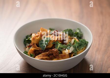 pâtes de fettuccine avec tomates séchées, flocons d'amande et feuilles de kale dans un bol blanc sur table en noyer Banque D'Images