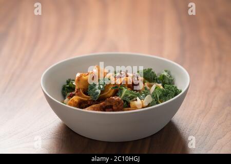 pâtes de fettuccine avec tomates séchées, flocons d'amande et feuilles de kale dans un bol blanc sur table en noyer Banque D'Images