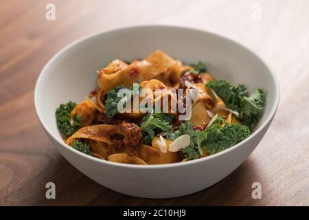 pâtes de fettuccine avec tomates séchées, flocons d'amande et feuilles de kale dans un bol blanc sur table en noyer Banque D'Images