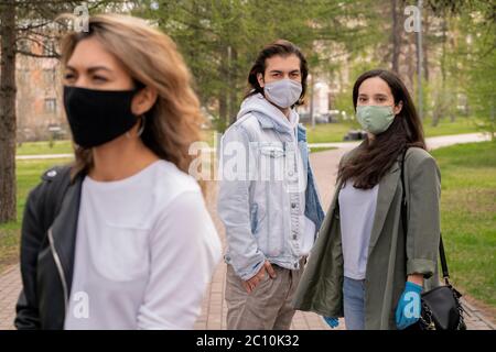 Jeune couple dans des masques faciaux regardant avec peur la femme traversant la rue pendant la pandémie de coronavirus Banque D'Images