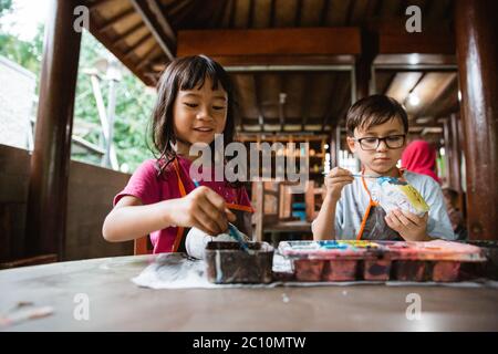 Une petite fille et un garçon qui font de l'artisanat et qui peint un objet en céramique à une table Banque D'Images