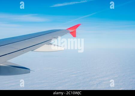 Aile d'avion contre le fond du ciel bleu clair et de la mer de nuages blancs denses en dessous. Banque D'Images