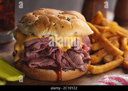 Sandwich au rôti de bœuf avec fromage cheddar et sauce barbecue sur un rouleau d'oignon sur une planche à découper en bois rustique Banque D'Images