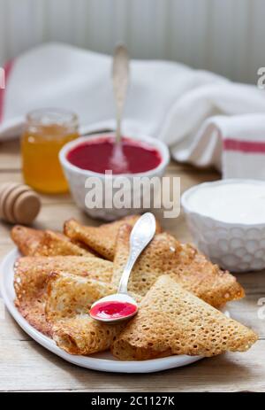 Crêpes au seigle et au grain entier servies avec de la crème aigre, du miel et de la sauce aux fraises. Style rustique. Banque D'Images