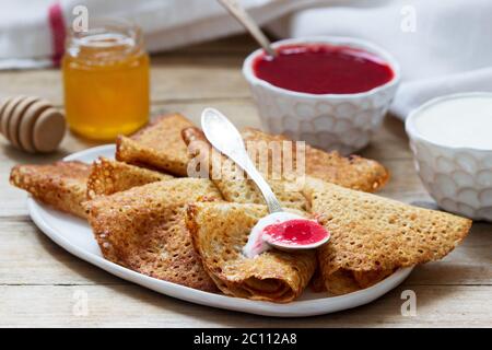 Crêpes au seigle et au grain entier servies avec de la crème aigre, du miel et de la sauce aux fraises. Style rustique. Banque D'Images