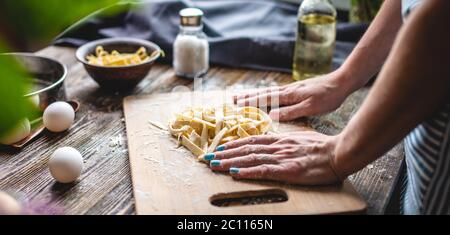 La femme saupoudrer soigneusement de farine sur des nouilles maison fraîches et crues. Concept de processus de cuisson des pâtes faites à la main dans une atmosphère chaleureuse Banque D'Images