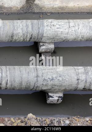 tuyaux d'eau, tôles de toiture isolées pendant la réparation dans un fossé rempli de liquide boueux Banque D'Images