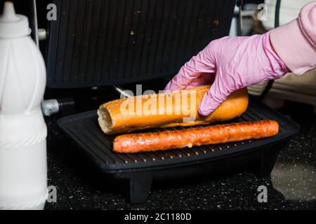 barman faisant un hot dog français avec des saucisses et rouler sur la surface du gril Banque D'Images