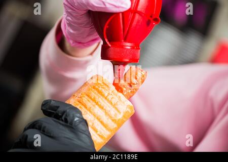 barman ajoutant de la sauce ketchup à un hot dog français avec saucisse grillée Banque D'Images