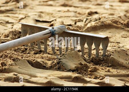 les outils de râteau reposent sur le sable, préparés pour poser des dalles de pavage. Banque D'Images