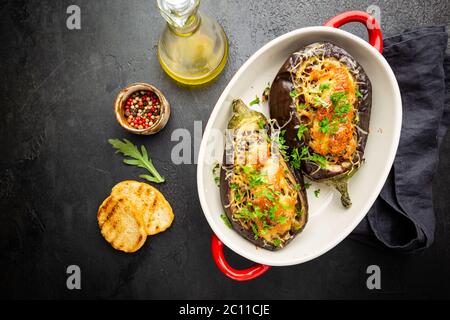 Aubergines ou aubergines cuites au four farcies de champignons, de légumes et de fromage sur fond noir, vue du dessus Banque D'Images