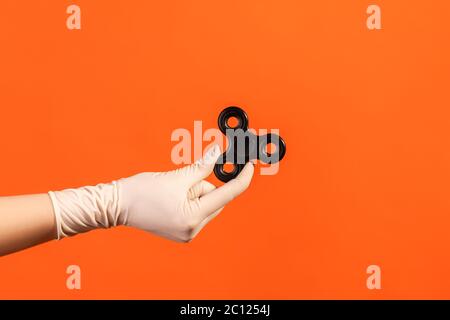 Vue latérale du profil de la main humaine en gants chirurgicaux blancs tenant un spinner de violon noir. Prise de vue en studio, isolée sur fond orange. Banque D'Images