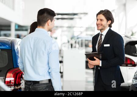 Vendeur proposant une voiture de couple debout dans la salle d'exposition Auto Banque D'Images