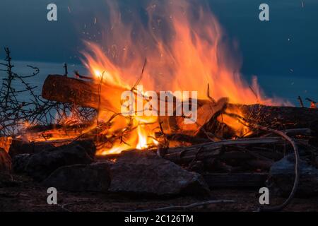 Feu de camp au crépuscule sur la plage. Gros plan sur le feu avec des étincelles et une onde de chaleur. Banque D'Images