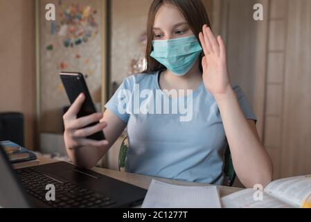 Une adolescente, dans un masque médical, la protection des bactéries des virus et des maladies, fait un appel vidéo sur un smartphone, e-éducation et leçons d'Internet Banque D'Images