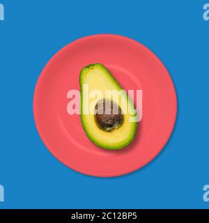 Avocat dans une assiette rouge sur fond bleu. Le concept de la cuisine végétarienne. Conception minimale Art. Banque D'Images