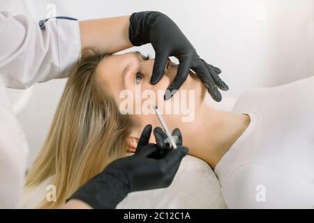 Traitement cosmétique. Gros plan des mains d'esthéticienne faisant l'injection de levage de peau faciale au visage de jeune femme, joues. Belle réception de la patiente Banque D'Images