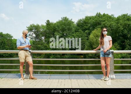 Homme et femme regardant dans différentes directions en gardant la distance à quelques mètres pour éviter la propagation du coronavirus près de la rivière. Guy et fille dans les masques de visage Banque D'Images