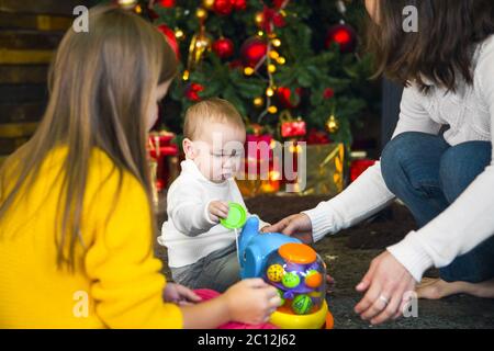 Une jeune mère et ses deux enfants ouvrent un cadeau de Noël par un arbre de Noël dans un salon confortable Banque D'Images