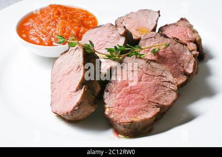 Portion de steak juteux avec sauce tomate sur un blanc plaque Banque D'Images